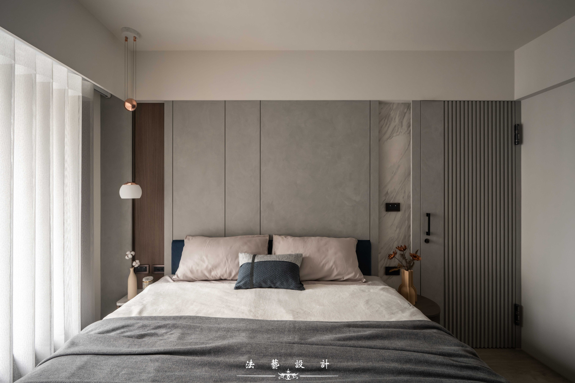 主臥室背牆同樣延續灰色調作為主視覺，透過深色木紋與石紋元素點綴，為空間注入沉穩而細膩的質感。隱藏門則以相同色系的灰色格柵設計，讓門片自然融入牆面，堆疊出豐富的層次變化。