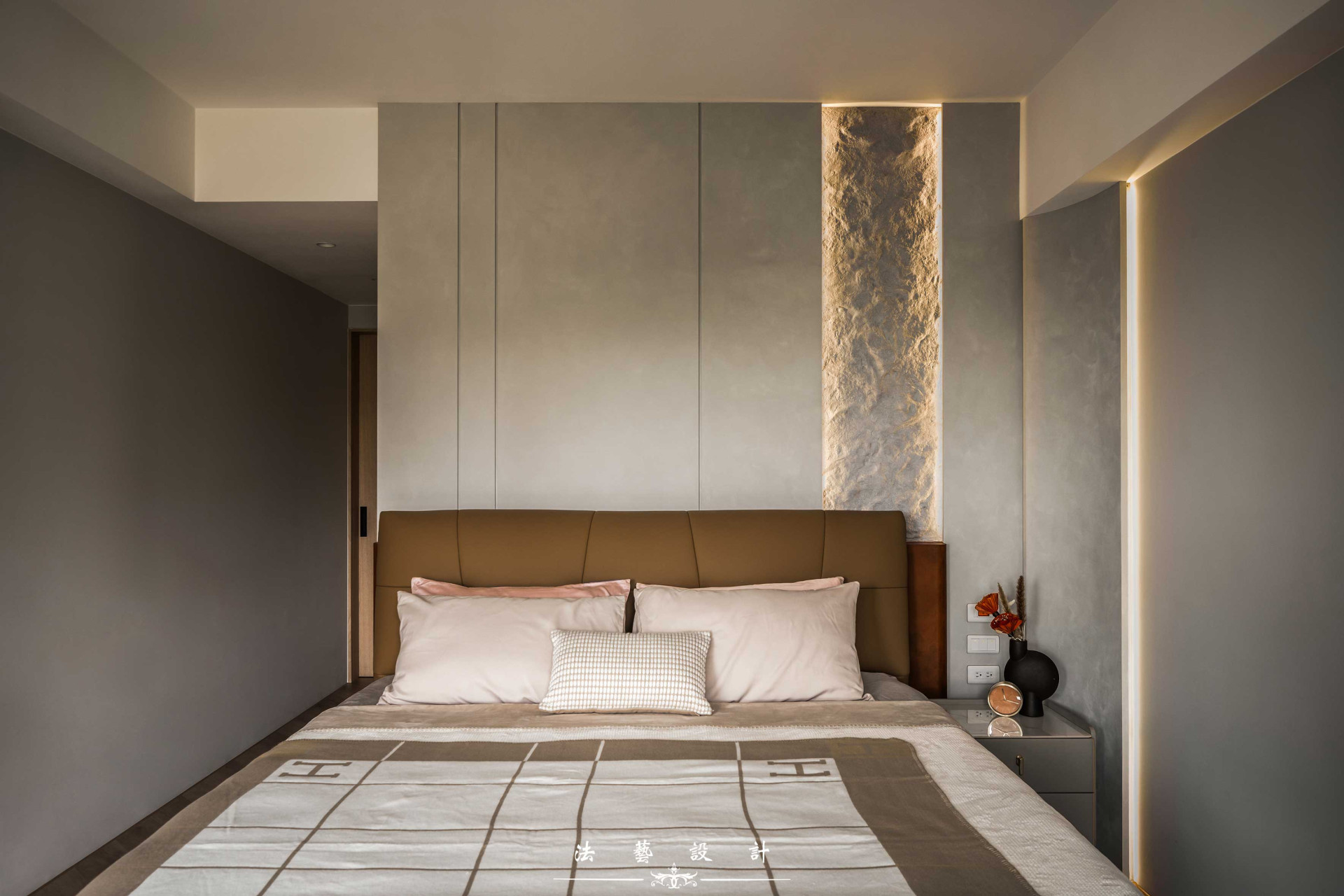 主臥最特別的就是床頭牆面的石皮設計，由資深師傅以純手工的方式一層層堆疊紋路，細膩呈現宛如真實石皮的自然紋理，並透過燈光映照，打造豐富的光影層次與細膩質感。
